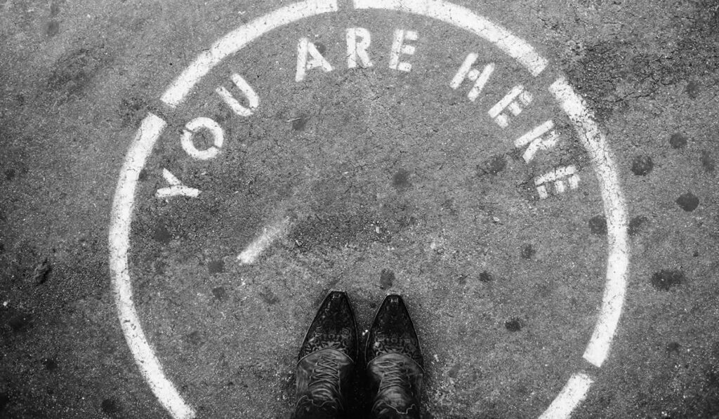Black boots standing on the ground in a painted circle with stenciled words: You Are Here